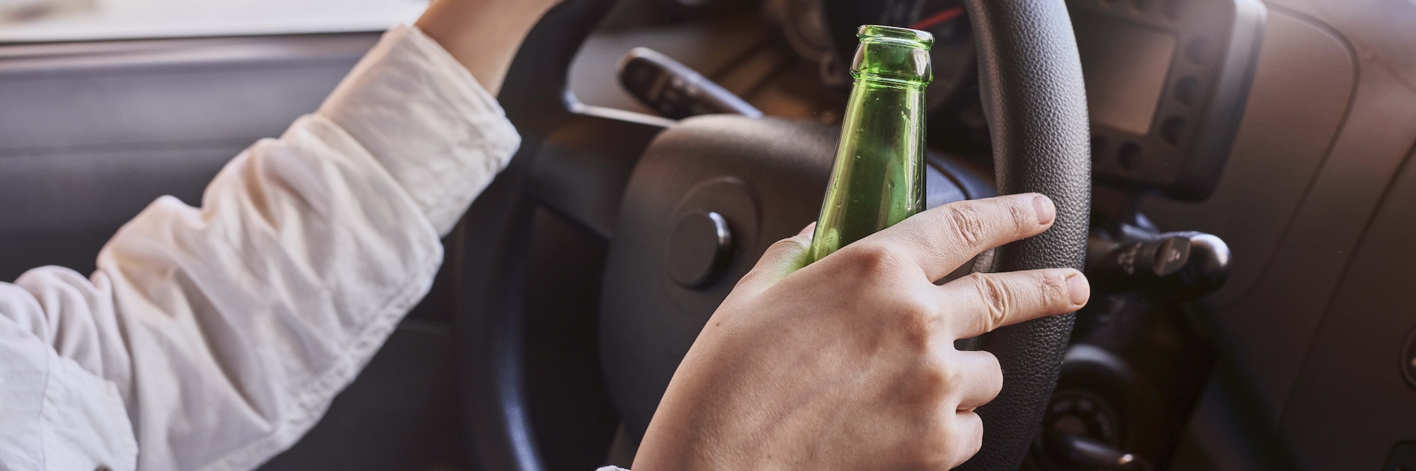 An unrecognizable female drinking beer while driving car. Concepts of driving under the influence drunk driving or impaired driving