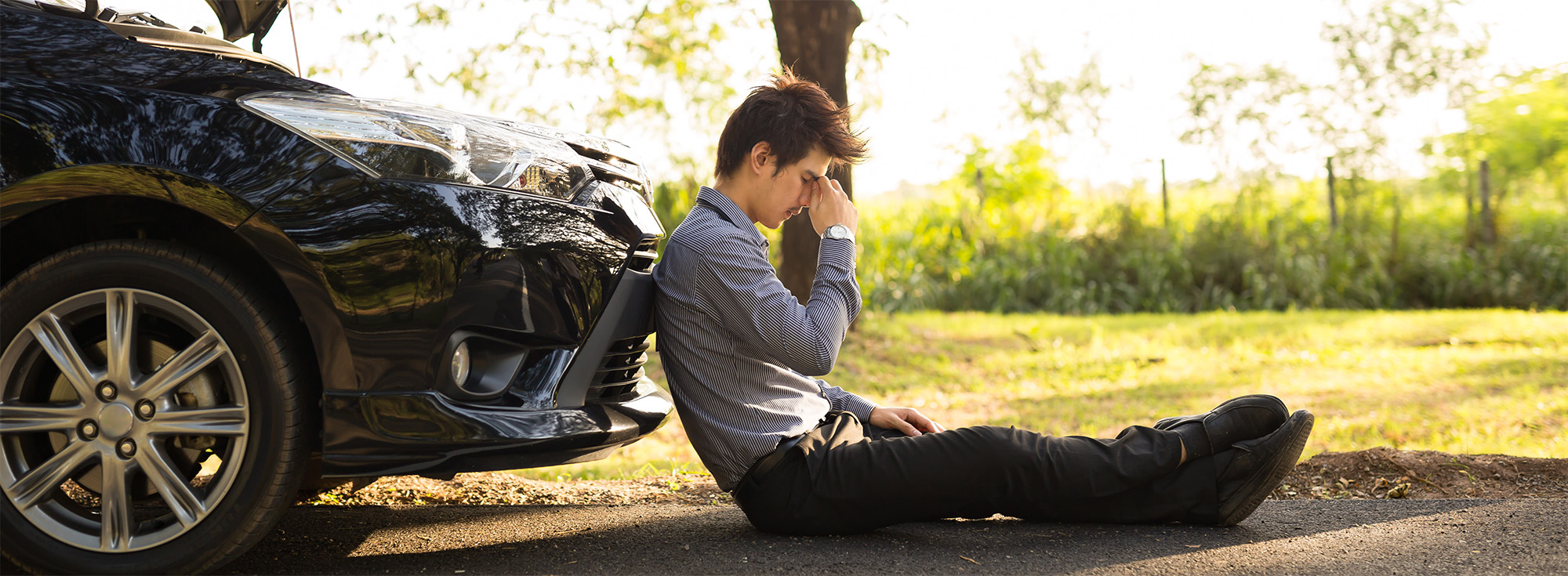 Full length of businessman with hands on head sitting by broken down car at countryside