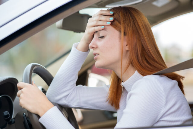 Sad tired yound woman driver sitting behind the car steering wheel in traffic jam.