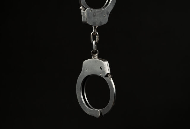 Locked police handcuffs on a black background with text / writing