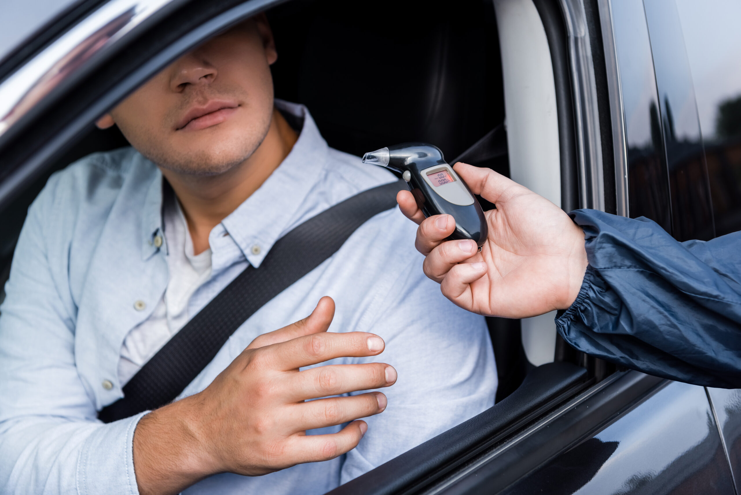 cropped view of driver taking breathalyzer from policeman while sitting in car.