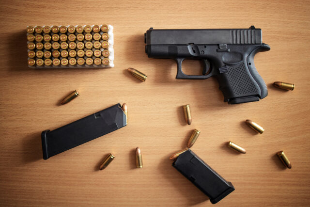 Gun with box of ammunition and bullets on wooden background. Semiautomatic handgun firearm with mags and rounds.