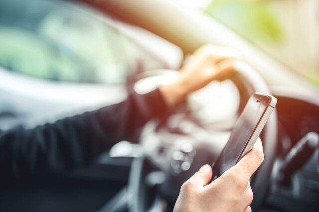 Woman looking at mobile phone while driving a car. Transportation and vehicle concept.