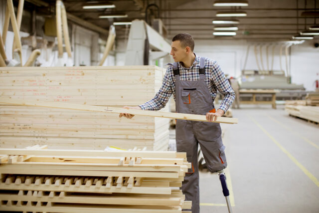 Disabled young man with an artificial leg is working at the furniture factory