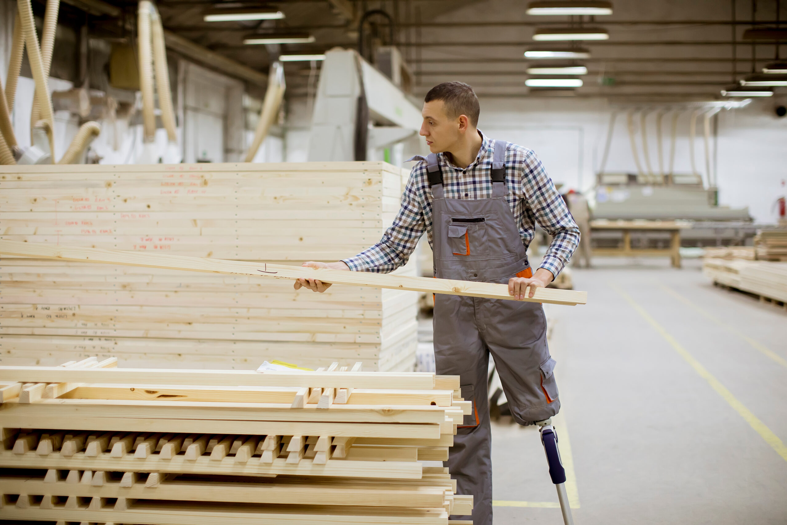 Disabled young man with an artificial leg is working at the furniture factory