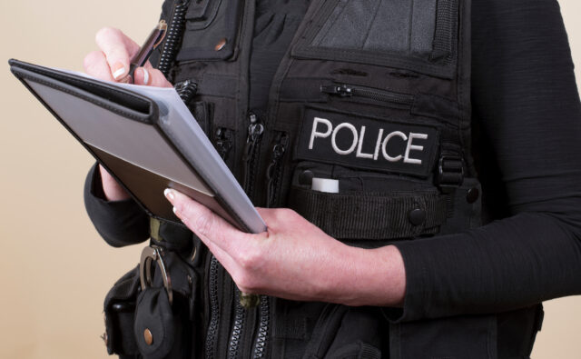 Police officer wearing tactical vest writing notes on a pad
